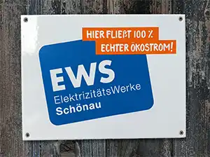Emailleschild mit Logo und Motto «Hier fließt 100 % Ökostrom» auf einer rustikalen Bretterwand