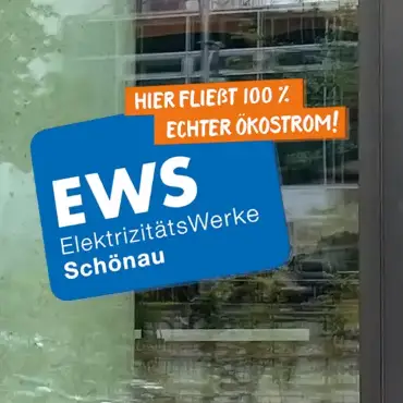 Ein EWS-Aufkleber auf einem Fenster mit Logo und dem Motto «Hier fließt 100% Ökostrom»