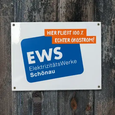 Ein Emailleschild mit Logo und dem Motto «Hier fließt 100% Ökostrom» auf einer rustikalem Bretterwand