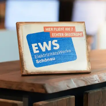 Ein Holzschild mit Logo und dem Motto «Hier fließt 100% Ökostrom» auf einem hölzernen Empfangstresen