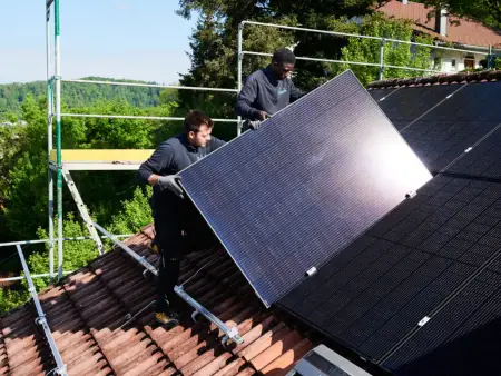 Ein Mann und ein Kind schauen fröhlich aus einem Dachfenster, vor ihnen eine PV-Dachanlage