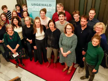 Eine Gruppe von rund zwei Dutzend Menschen schaut nach oben in die Kamera, im Hintergrund auf einem großen Plakat der Text «Urgewald – Auf den Spuren des Geldes».