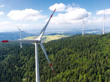 Vier Windkraftanlagen auf einem bewaldeten Berg