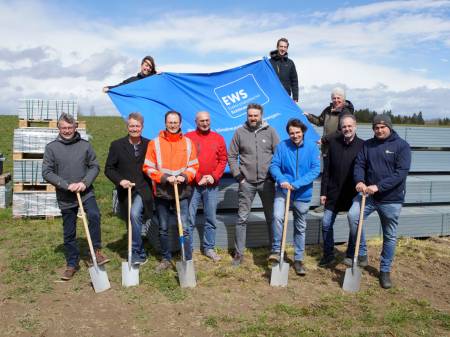 Gruppe steht mit Spaten vor einem Banner der EWS und Stahlträgern