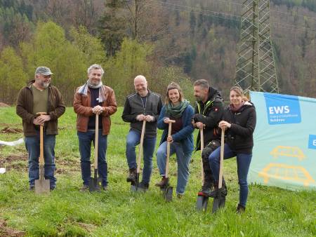 Gruppe von sechs Menschen mit Spaten nebeneinander neben einem Banner