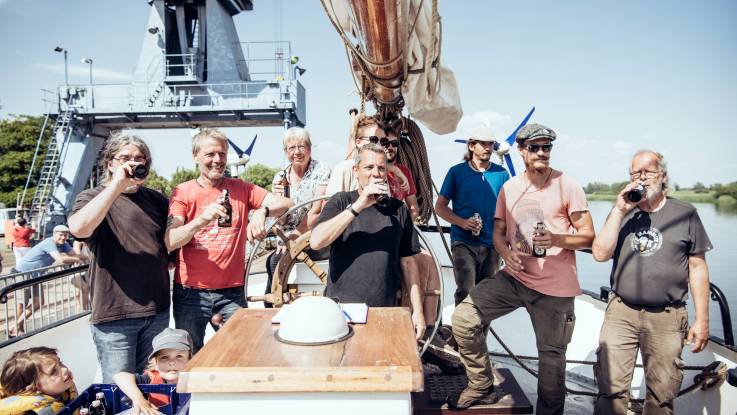 Gutgelaunt steht die Mannschaft des Schiffes zu zehnt auf Deck und labt sich an einem kühlen Fläschchen Bier.