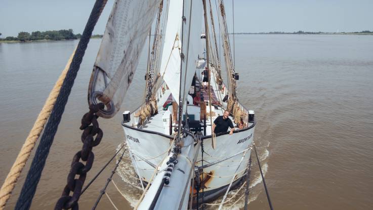 Aufnahme eines Segelschiffes vom Bugspriet aus; von der Reling her grinst ein Mann gutgelaunt in die Kamera.