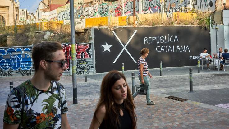 Two young people walk in front of a black banner with a large X on it.