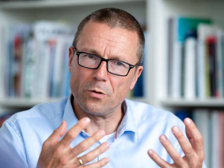 Brustportrait eines Mannes mit Brille und Hemd, der erläuternd die Hände hebt