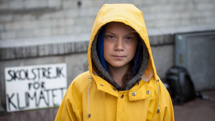 Ein Mädchen in einer gelben Regenjacke, im Hintergrund ein Schild mit der Aufschrift: "Skolstreik for Klimatet"