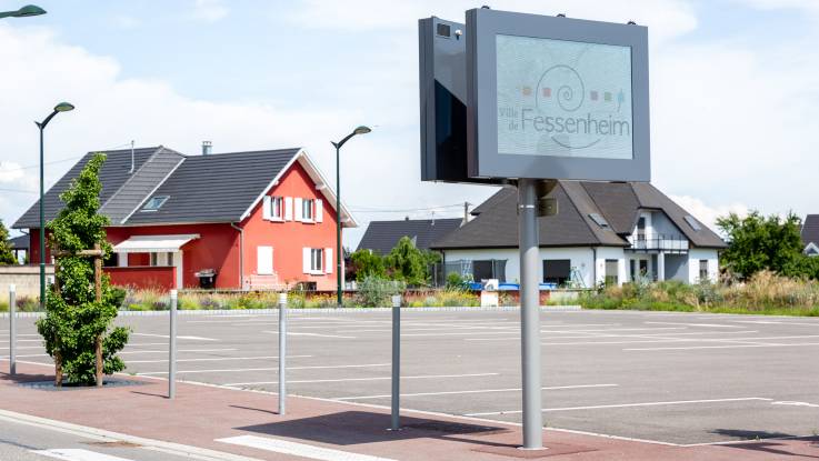 Ein Parkplatz, ein Fußweg, zwei Einfamilienhäuser, eine Anzeigetafel: alles sieht sehr neu und propper aus.