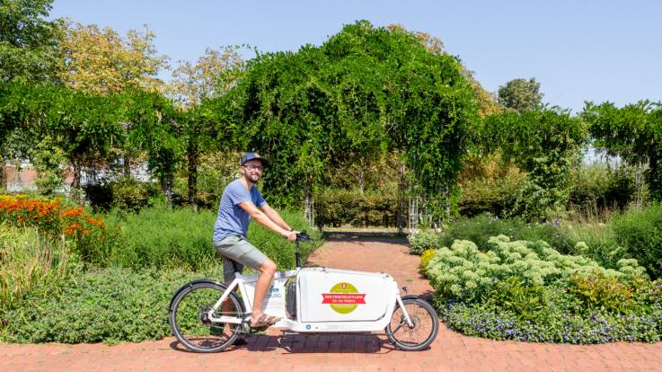 Ein junger Mann im Hochsommer auf einem Lastenfahrrad in einem Park