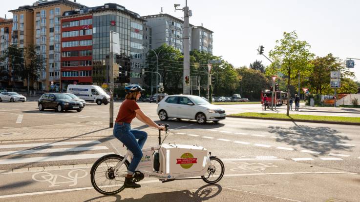 Eine junge Frau ist mit einem Lastenrad im Stadtverkehr unterwegs.
