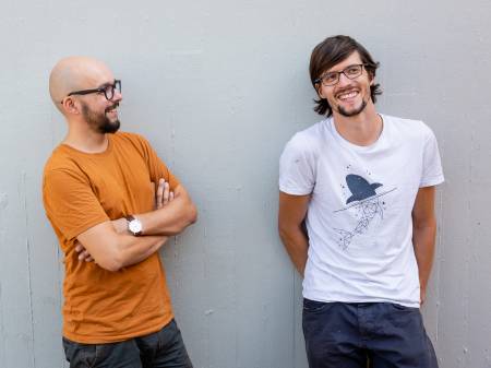 Zwei junge Männer im Sommer, lachend vor einer Wand