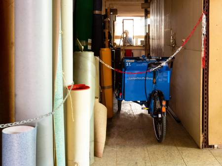 Ein Lastenrad steht geparkt neben Teppichrollen.