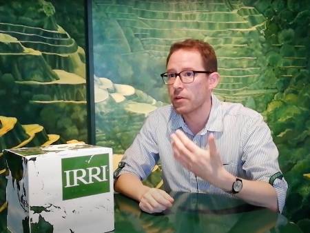 Ein rothaariger, etwa 40 Jahre alter Mann mit Brille sitzt an einem Tisch und referiert.