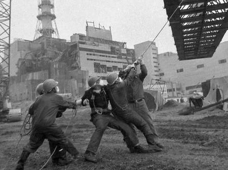 Eine Gruppe Männer zieht vor der Ruine des AKW Tschernobiyl an einem Seil, das an einem über ihnen schwebenden Stahlträger befestigt ist.