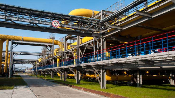 An einer Straße erstreckt sich eine große industrielle Anlage mit bunt lackierten Rohrsystemen bis zum Horizont.
