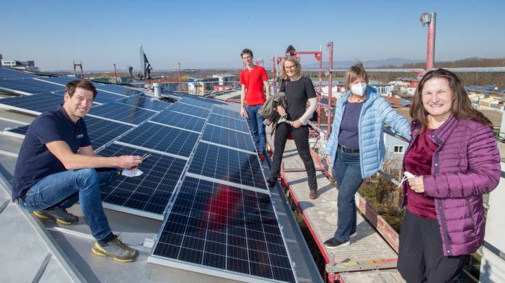 Auf einem Dach das mit Solarpanelen bestückt ist, steht eine Gruppe von Leuten.