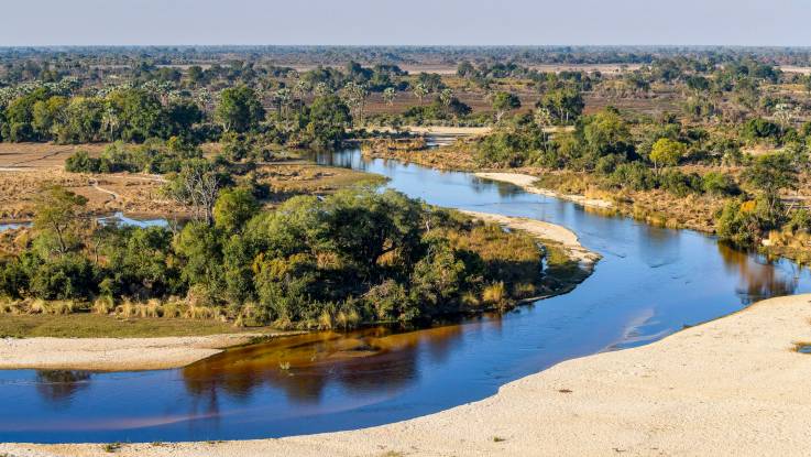Durch eine weitläufige flache Landschaft schlängelt sich ein Fluss.