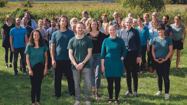 Ein sommerliches Gruppenfoto auf dem Land zeigt eine Gruppe von mehr als fünfundzwanzig, in der Hauptsache jungen, Menschen.