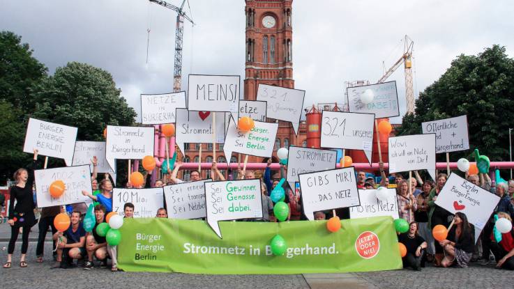 Group photo in front of the Rotes Rathaus in Berlin. Some 40 people are holding several speech-bubble signs displaying various slogans.