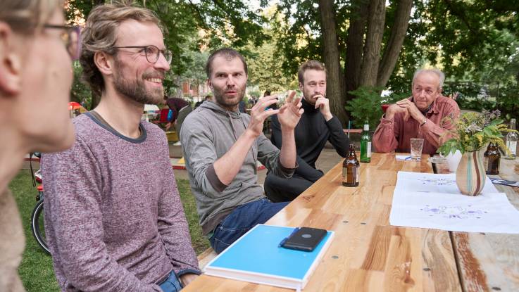 A group of five people are having a discussion around a garden table in summer.