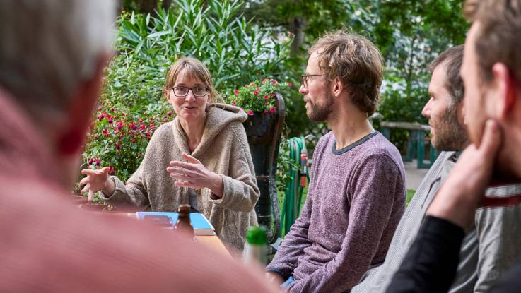 A group of young people are having a discussion around a garden table in summer.