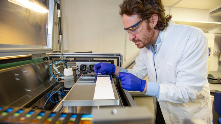 Jan-Hendrik Hehemann legt konzentriert einen Objektträger aus dünnem Glas auf einen technischen Apparat. 