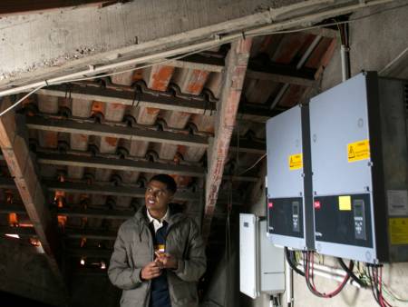 Alekson Dias da Luz stands on the roof. In front of him, we see solar transformers. 