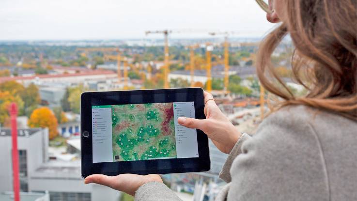 Vor einer Großbaustelle hält einer Frau ein ipad mit einem Stadtplan ins Bild.