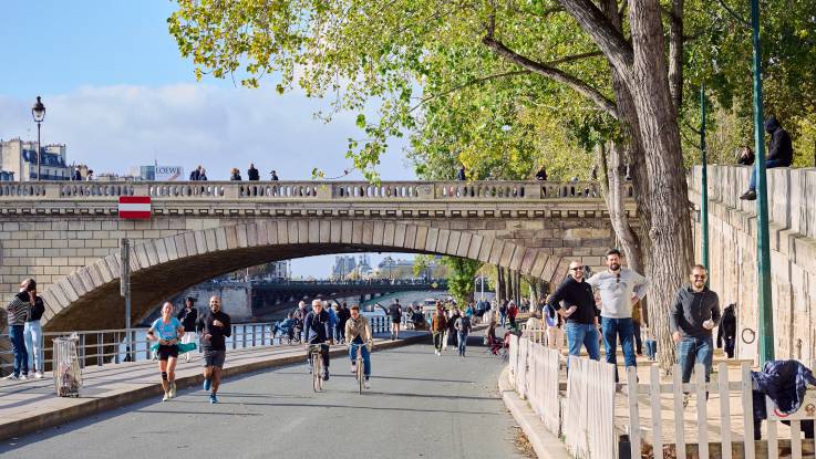 Am Ufer der Seine sind im Sonnenschein viele Fußgänger und Radfahrer unterwegs.