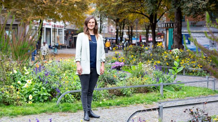 Eine junge Frau steht auf einem sommerlichen, mit Blumen bepflanzten Platz.