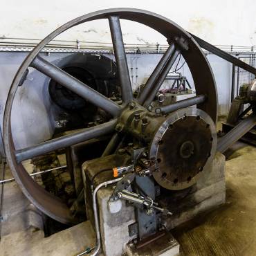 Das Schwungrad einer Wasserturbine: im Innern sind sieben Speichen angeordnet, seitlich geht ein Keilriemen ab. 