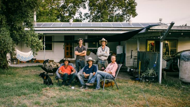 Eine Familie und deren Hunde posieren freundlich vor einem Haus – auf dem Wellblechdach sind PV-Module installiert.