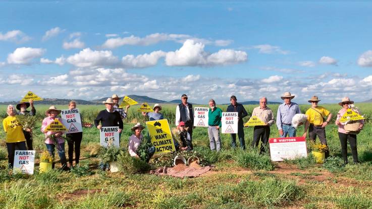 Eine Gruppe von älteren Männern und Frauen, alle mit Protestplakaten gegen weitere Gasförderungen ausgestattet, posieren zu einem Gruppenfoto auf dem Feld.