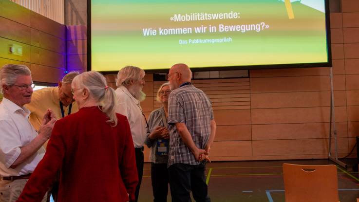Abseits der Bühne stehen einige Personen in vertrauter Pose beieinander und unterhalten sich.