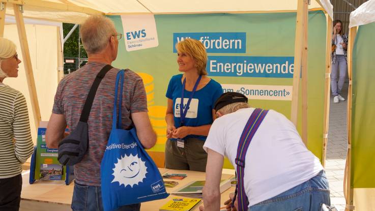 Hinter dem Stand der EWS horcht eine blonde Frau aufmerksam den Fragen der Besucher.   