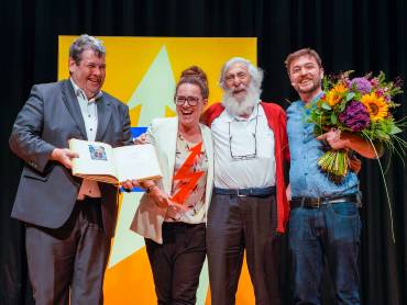 Eine junge Frau in weiter Kleidung und hochgesteckten Haaren spricht auf dem Podium.  