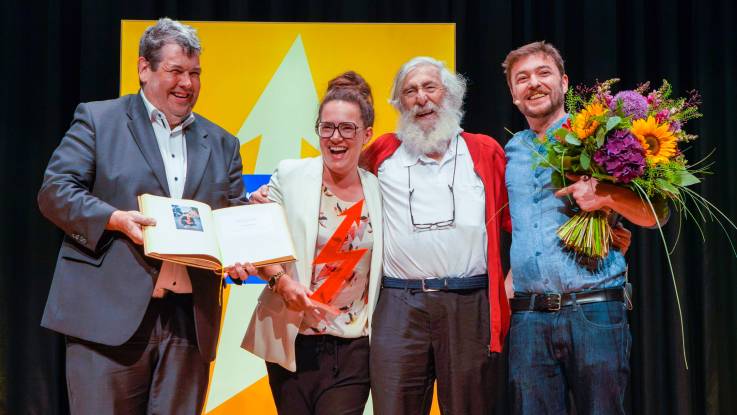 Vor der gelben Stele stehen Bürgermeister Schelshorn mit Katja Diehl, Michael und Sebastian. Die drei umarmen sich und alle lachen herzlich.