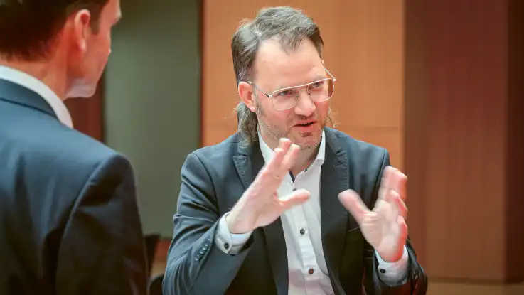 Ein Mann mit grau meliertem Bart unterhält sich mit seinem Gegenüber und gestikuliert dabei mit seinen Händen.