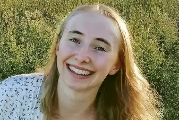 Porträtaufnahme: Eine junge Frau mit offenen, blonden Haaren blick mit breitem Lächeln in die Kamera.
