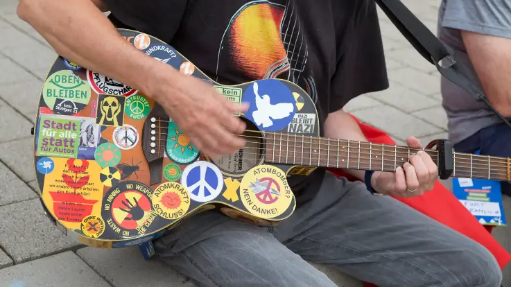 Nahaufnahme: Jemand spielt auf einer Gitarre, die mit einem Mosaik aus bunten Stickern beklebt ist. 