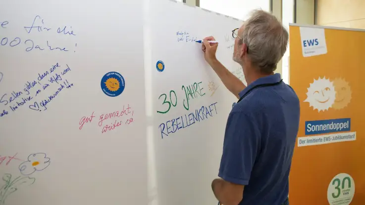 Ein Mann schreibt mit einem Filzstift seine Widmung auf ein Wandplakat mit der Überschrift: 30 Jahre Rebellenkraft.