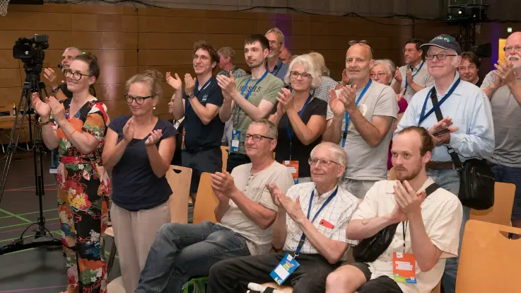 Viele Personen in den ersten Reihen stehen applaudierend vor der Bühne und schauen wohlwollend nach vorne. 