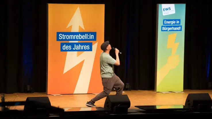 Ein Mann mit Schiebermütze nimmt auf der Bühne eine kuriose Pose ein: halb in die Knie gehend, schaut er nach oben. 